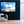 Modern living room with large sunrise sky photography wall art, cozy white chair, and potted plant.