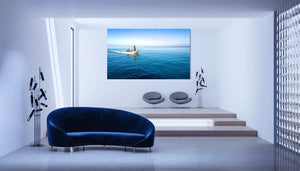 Modern living room with blue velvet sofa and large wall art of people boating on calm blue water