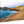 Acrylic photo print of a rocky coastline with blue ocean waves and distant buildings at sunset