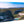 Glossy aluminum wall art print featuring a scenic landscape with lush green hills, a small bay, and a distant house.