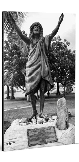Black and white photo of a joyful statue with arms raised in tropical outdoor setting.