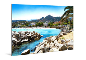 Aluminum photo print of a sunny beach scene with blue water, palm trees, and rocky shoreline.