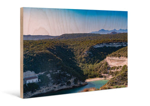 Artistic landscape photo print on wood showing forested hills, small bay, and blue sky.
