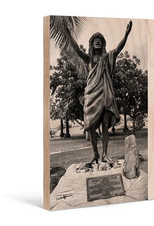 Direct print on wood of a statue with arms raised, tropical trees in background, outdoor setting