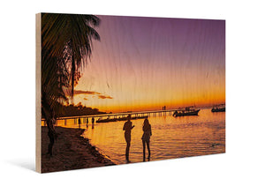Sunset beach scene with silhouettes, palm tree, pier, and boats printed on wood panel