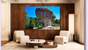 Modern living room with two beige chairs, marble coffee table, and large landscape wall art featuring a mushroom-shaped rock formation in nature.
