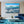Modern living room with blue velvet sofa, ocean landscape wall art, and wood shelving