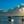 Serene coastal scene at sunset with boats on calm water, dramatic clouds, and a child wading.