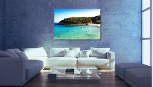 Modern living room with a white sofa, glass table, and coastal landscape wall art.