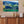 Framed landscape wall art of green mountains and lake above a wooden sideboard with decor