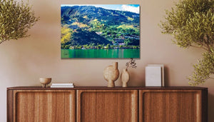 Framed landscape wall art of green mountains and lake above a wooden sideboard with decor