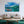 Modern living room with wooden furniture and a large wall art of a boat on a lake with green hills