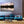 Modern living room with teal sofa, glass table, nature wall art, and fireplace