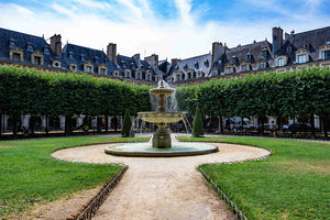 image représentant une fontaine, le jardin et les façades de la place des Vosges à Paris sous un ciel bleu