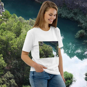 Woman wearing white t-shirt with landscape print, standing by scenic river and lush green trees