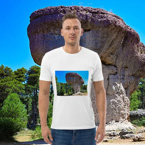 Man wearing a white t-shirt with a scenic rock formation print, standing outdoors by a large mushroom-shaped rock and green trees under a blue sky