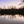 Calm lake at sunset with tree reflections and buildings in the background