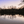 Serene lake at dusk with bare trees reflected in calm water and pastel sunset sky.