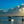 Serene seascape at sunset with boats, dramatic clouds, and a person standing in shallow water.