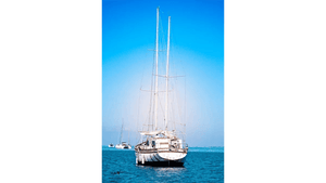 White sailboat with tall masts anchored on calm blue sea under clear sky