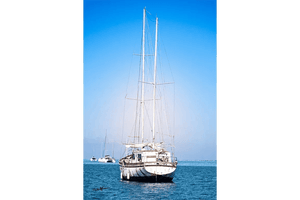 White sailboat on calm blue sea under clear sky, distant boats in background