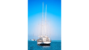 Sailboat anchored on calm blue sea under clear sky, with distant boats in background