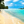 People walking on a tropical beach with palm trees, blue ocean, and a bright sky