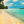 People walking on a tropical beach with turquoise sea, palm trees, and blue sky
