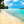 People walking on a tropical beach with turquoise water, palm trees, and blue sky