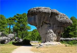 Large mushroom-shaped rock formation in a forest under clear blue sky