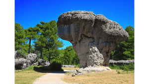 Mushroom-shaped rock formation surrounded by green trees under a clear blue sky
