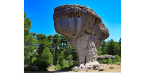 Large mushroom-shaped rock formation surrounded by green forest under clear blue sky