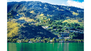 Green mountainside with houses overlooking a turquoise lake under a blue sky
