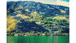 Green mountain landscape with scattered houses and trees overlooking calm lake water