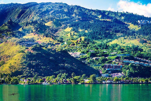 Colorful landscape photo of green mountains, forest, and waterfront houses on a sunny day
