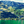 Vibrant green hillside with scattered houses and clear turquoise lake under blue sky