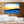 Modern living room with framed ocean sunset art print, minimalist sofa, and bonsai tree