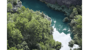 Aerial view of a turquoise river surrounded by lush green trees and rocky cliffs