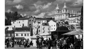 Black and white cityscape with statue, historic church, and people in a lively square