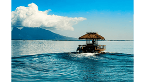 Tropical hut boat cruising on blue ocean with mountains and clouds in the background