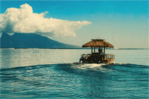 Tropical wooden hut boat on calm blue ocean with distant island and clouds