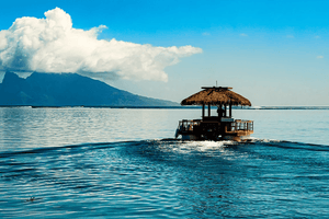 Tropical raft with thatched roof on calm blue sea, mountain and cloud in background
