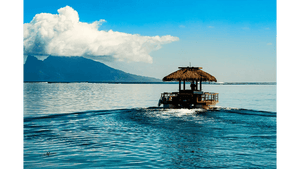 Tropical hut boat on calm blue sea with mountains and clouds in the background