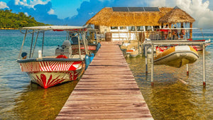 Colorful boats docked at a wooden pier leading to a thatched-roof hut over clear water