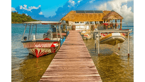 Wooden dock with colorful boats and thatched-roof hut over clear tropical water