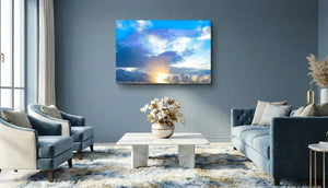 Modern living room with blue sofas, marble coffee table, and large sunrise cloudscape wall art.