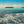 Tropical ocean scene with small islands, blue sky, turquoise waters, and distant clouds
