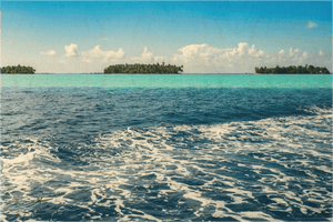 Tropical ocean scene with small islands, blue sky, turquoise waters, and distant clouds