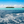 Tropical island with palm trees, blue ocean waves and bright sky under clouds