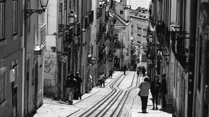 Black and white photo of a narrow European street with tram tracks and pedestrians